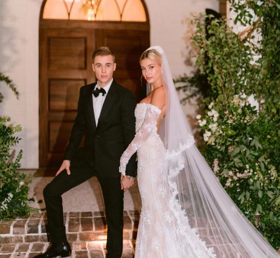 Justin e Hailey Justin e sua esposa Hailey Bieber em seu casamento. Justin Bieber está usando um terno preto e sua esposa um vestido de noiva longo e branco.