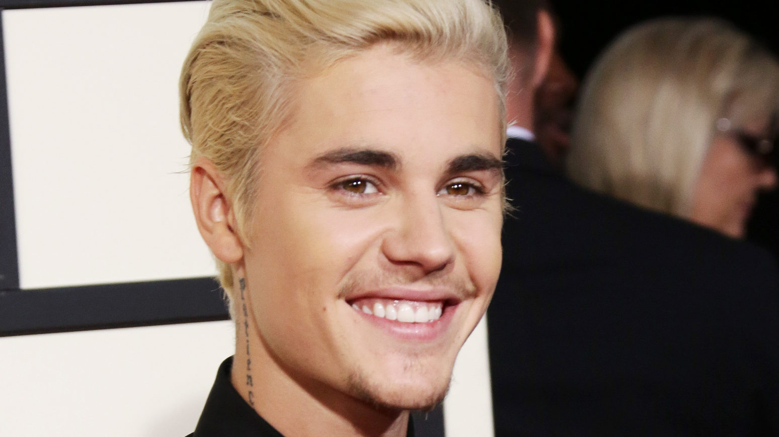 Justin Bieber pousando para os fotógrafos no Grammy Awards, sorrindo, terno preto, cabelo loiro