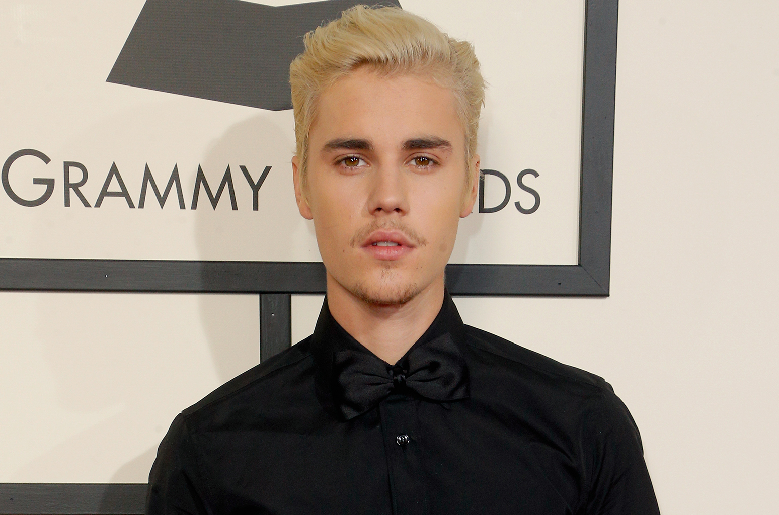 Justin Bieber pousando para os fotógrafos no Grammy Awards, sério, terno preto, cabelo loiro