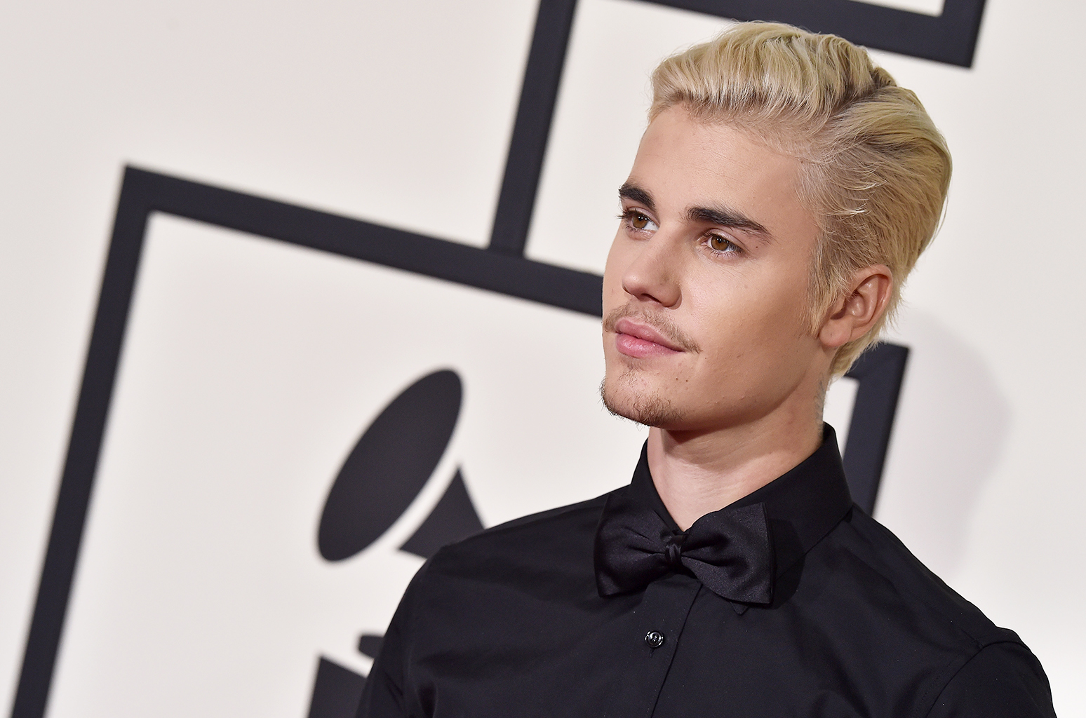 Justin Bieber pousando para os fotógrafos no Grammy Awards, sério, terno preto, cabelo loiro
