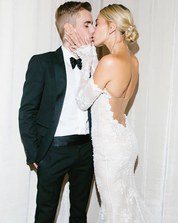 Justin e Hailey Justin beijando sua esposa Hailey Bieber em seu casamento. Justin Bieber está usando um terno preto e sua esposa um vestido de noiva longo e branco.